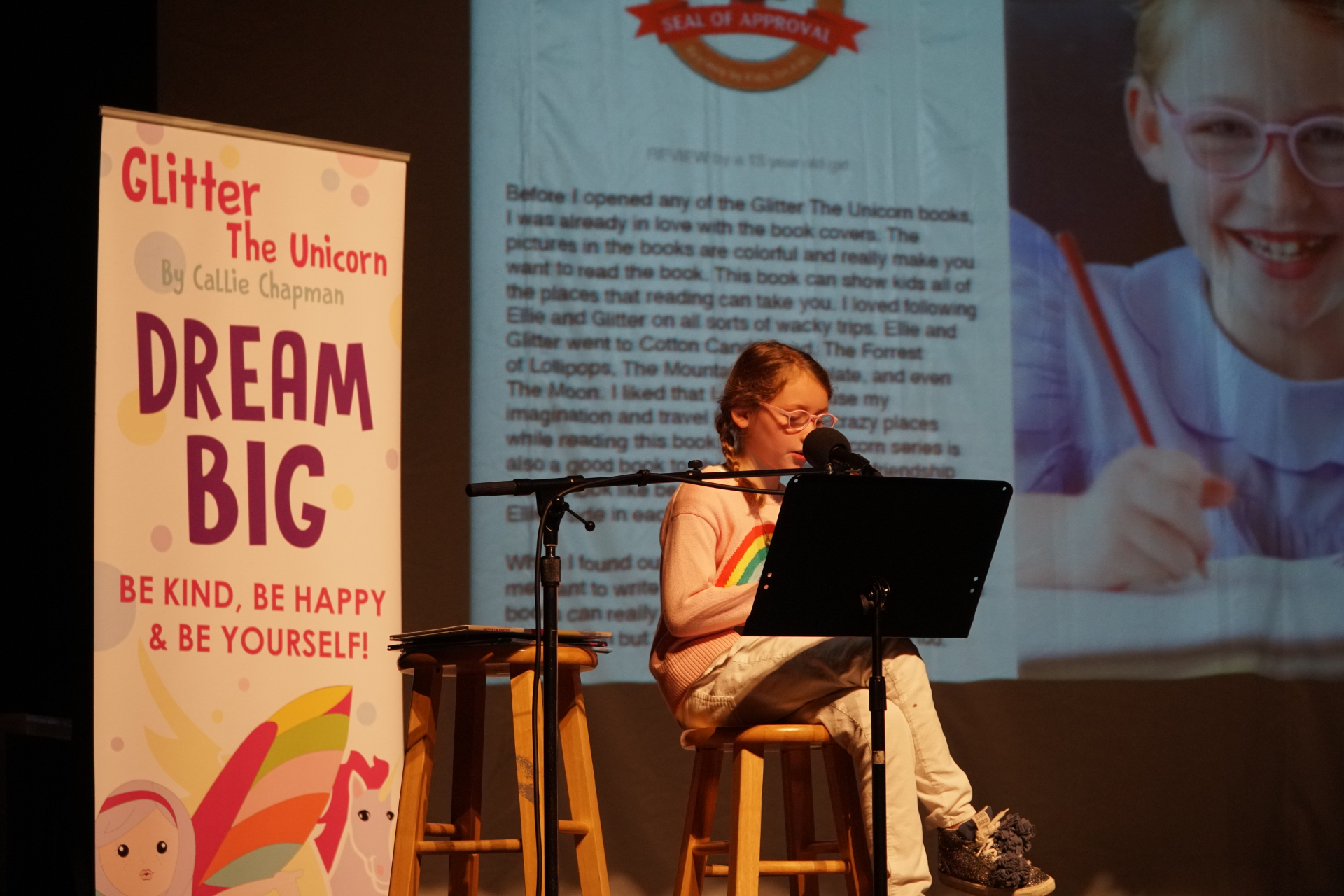 Reading from the Glitter the Unicorn series on stage with the Mom's Choice Seal of Approval banner
