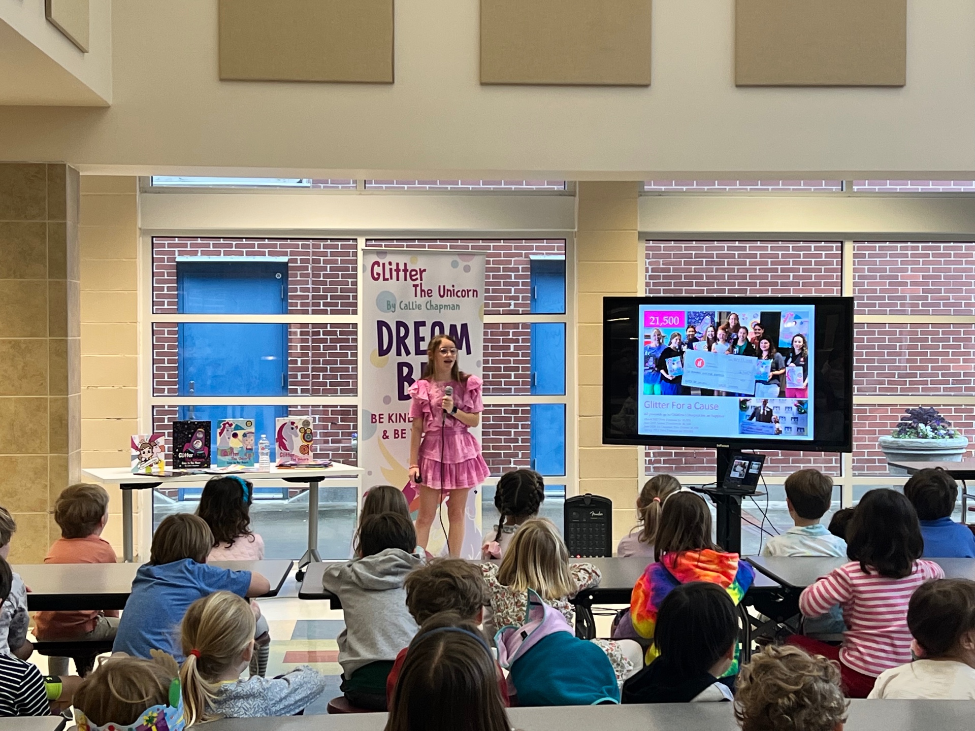 Speaking to students with the Glitter for a Cause $21,500 impact slide on screen